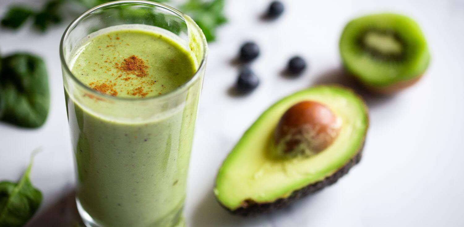 A glass of green smoothie next to an avocado.