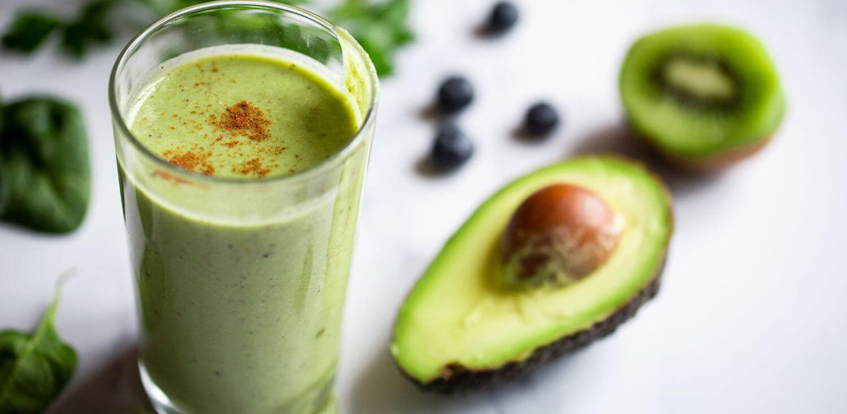 A glass of green smoothie next to an avocado.