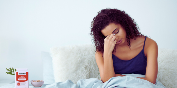 A woman sitting on a bed holding her hand to her face.