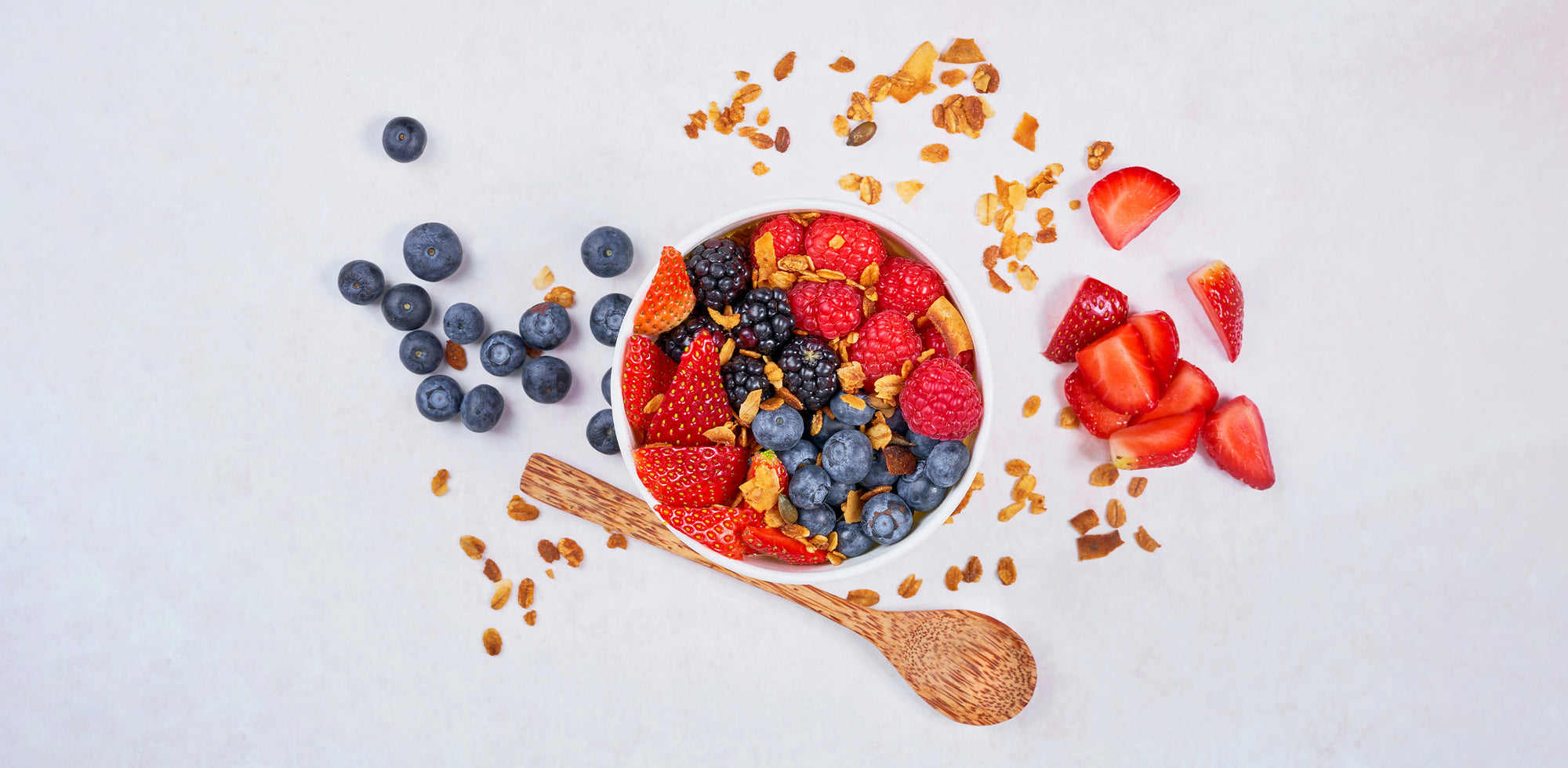 A bowl of cereal, strawberries, blueberries, and strawberries