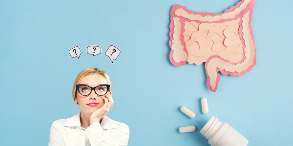 A woman with blonde hair and glasses looks up thoughtfully at question mark symbols. To her right is a cutout illustration of the human intestines, and below that are white pill capsules spilling from a bottle.