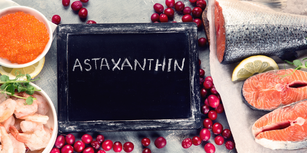 "ASTAXANTHIN" written on a chalkboard, surrounded by salmon, shrimp, fish roe, and red berries.