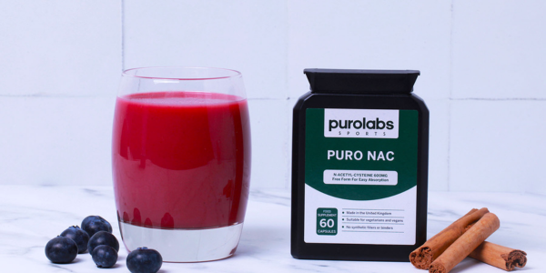 Glass of red juice beside blueberries, cinnamon sticks, and a Purolabs “PURO NAC” supplement bottle.