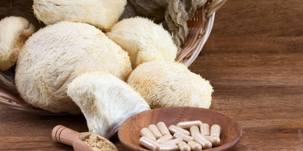Lion's Mane mushrooms and capsules in a wooden bowl on a table.