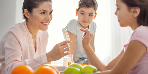 A woman sitting at a table gives vitamins to her kids