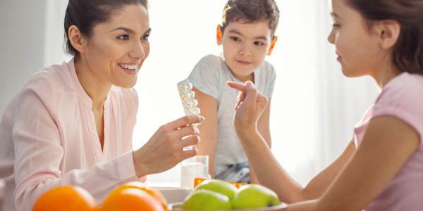 A woman sitting at a table gives vitamins to her kids 