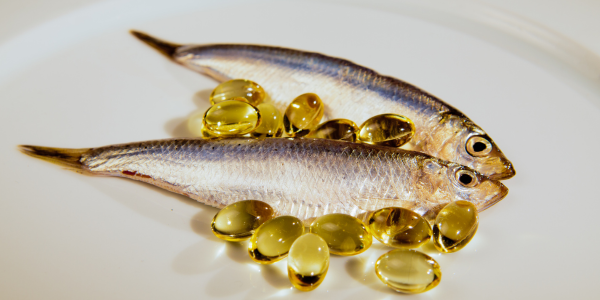 Two small fish placed alongside golden omega-3 supplement capsules on a white surface.