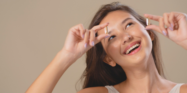 Smiling woman holding two capsules playfully near her face.