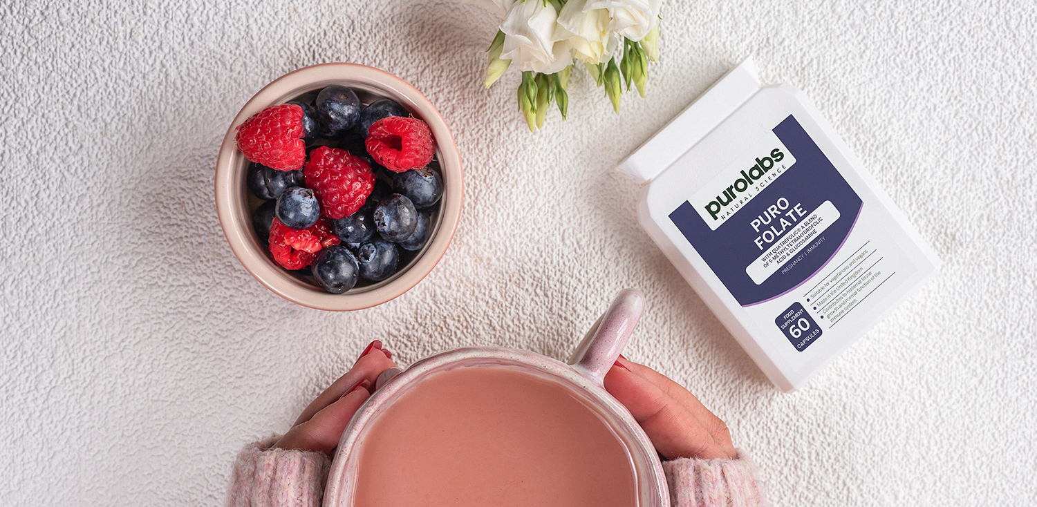 A bowl of berries, and a tea cup next to a supplement bottle.