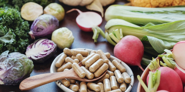 A bowl of pills next to a bowl of vegetables