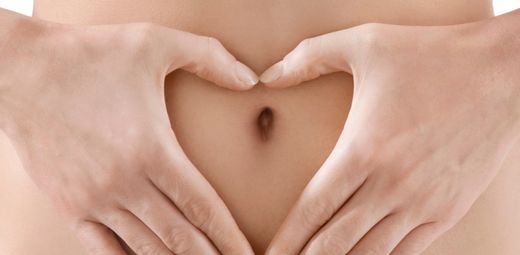 A woman's hands making a heart shape on her belly.