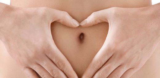 A woman's hands making a heart shape on her belly. 