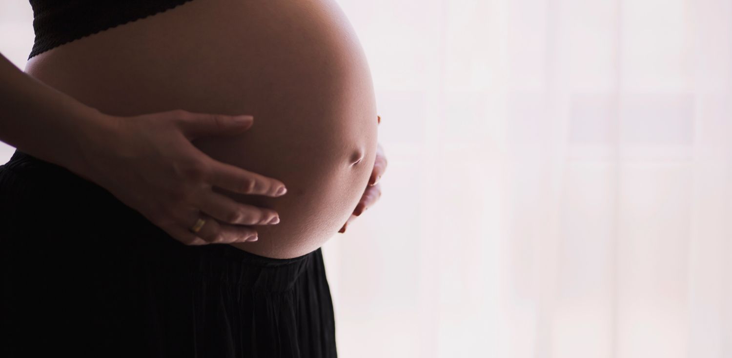 A pregnant woman in a black dress holding her belly