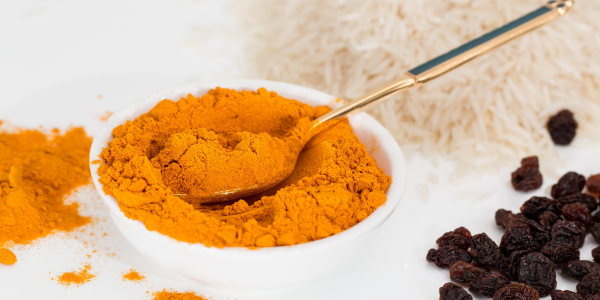 A white bowl filled with orange colored turmeric powder next to raisins