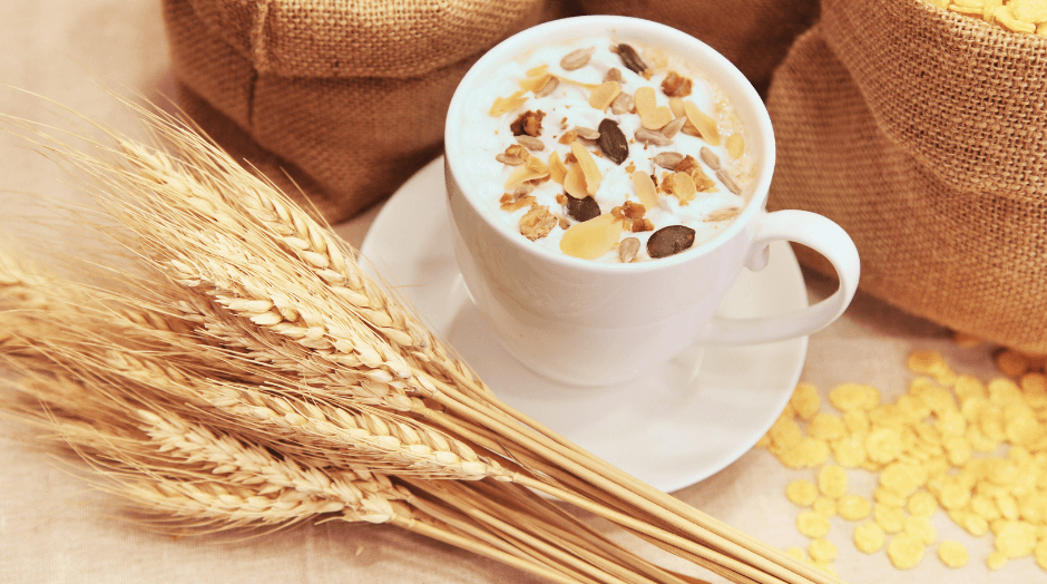 A cup of cereal sits on a saucer next to a sack of grain.