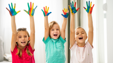 3 smiling kids raise their painted hands to the sky