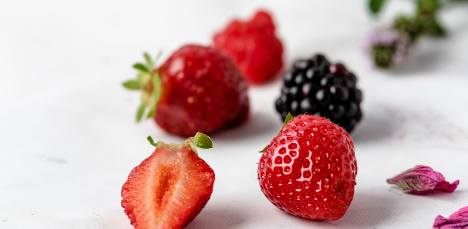 A group of strawberries and raspberries on a white surface.