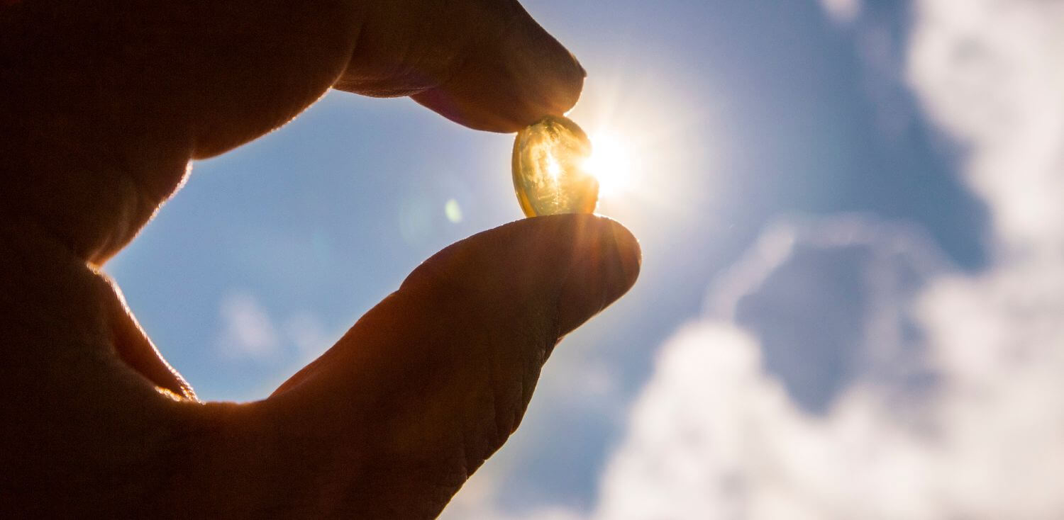A person holding a pill in their hand pointing to the sun.
