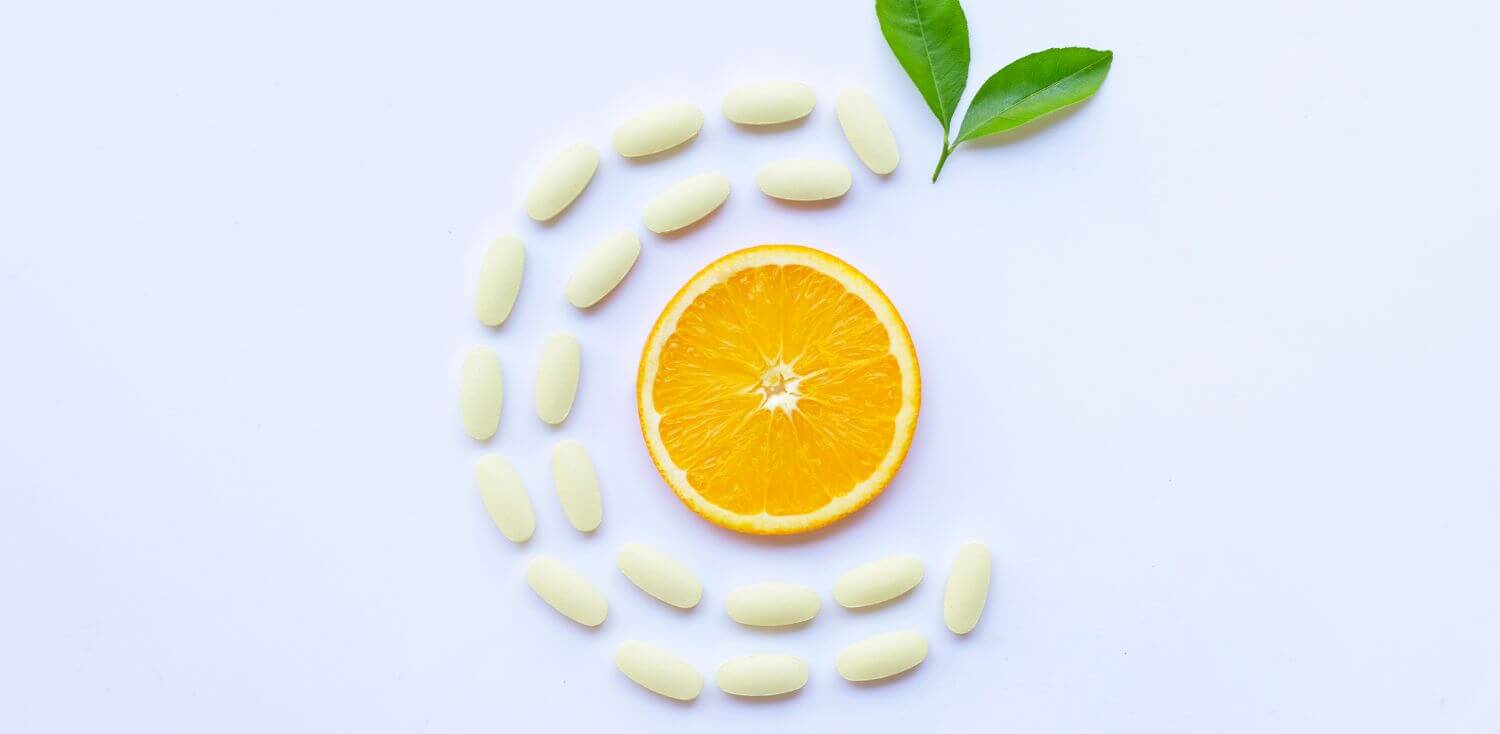 A sliced orange and some pills organised in the form of letter C sitting on top of a white table