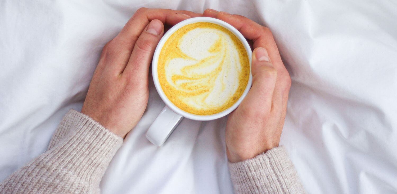 A person holding a cup of turmeric latte in their hands.