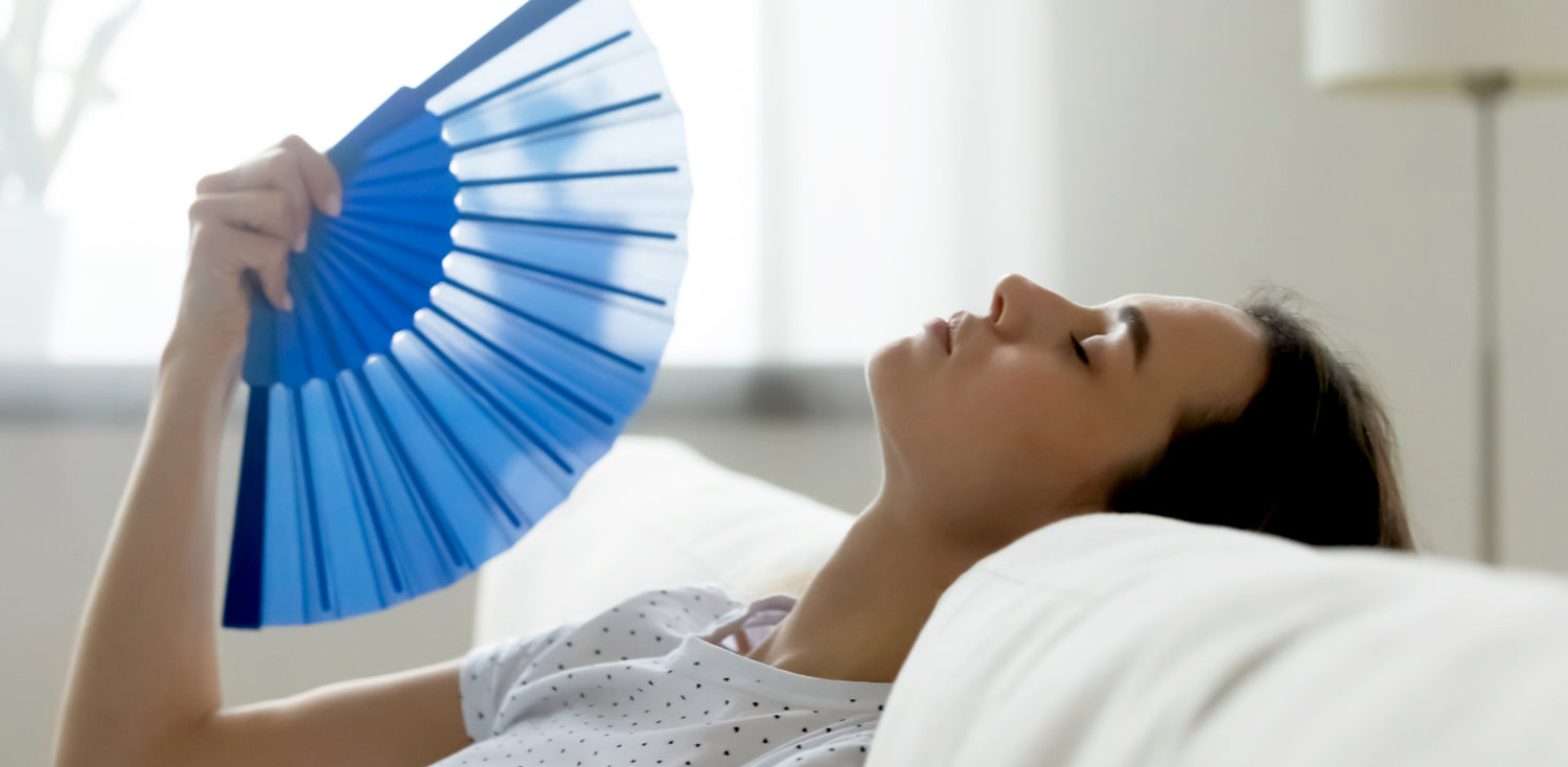 A woman laying on a bed holding a blue fan.