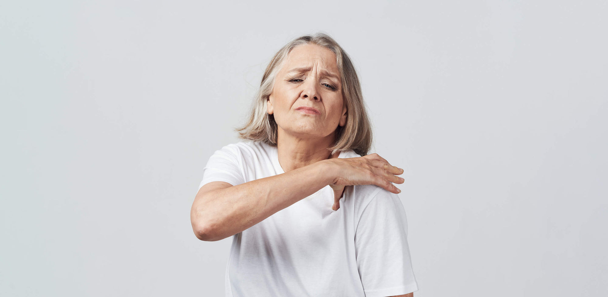 A woman holding her hand on her aching shoulder.
