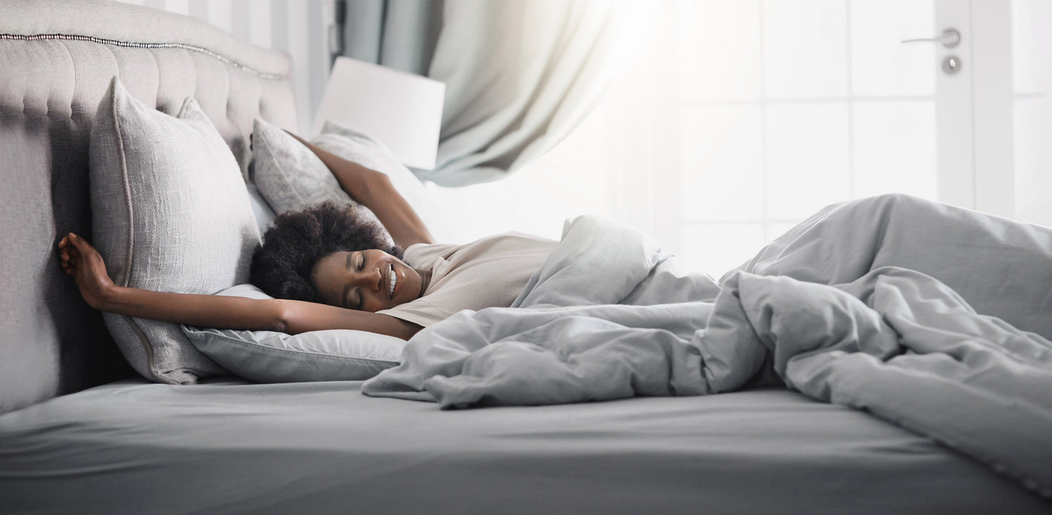 A woman waking up laying on a bed with a white comforter.