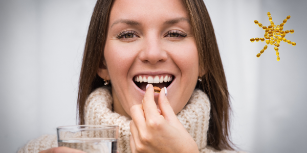 A woman smiling and holding a glass of water and taking a Vitamin D capsule
