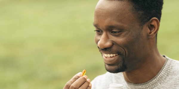 A man smiles while holding a small capsule supplement.
