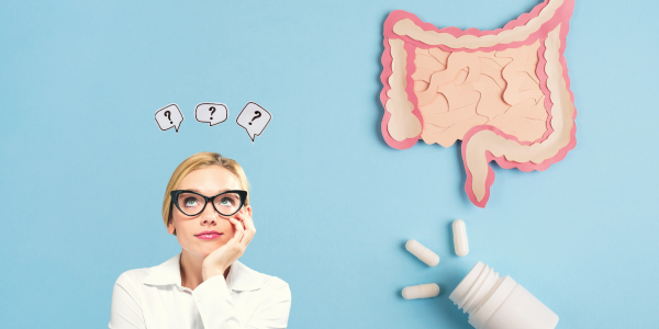 A woman with blonde hair and glasses looks up thoughtfully at question mark symbols. To her right is a cutout illustration of the human intestines, and below that are white pill capsules spilling from a bottle. 