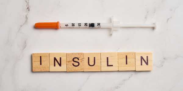 Syringe above wooden letter tiles spelling “INSULIN” on a light marble surface.