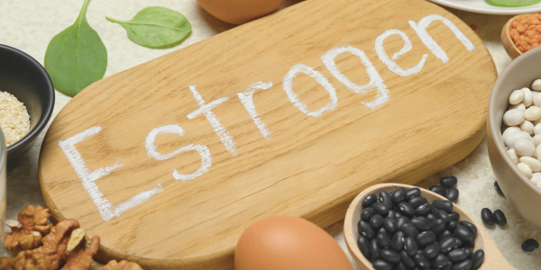 Wooden board with the word 'Estrogen' surrounded by foods like beans, eggs, nuts, and spinach.
