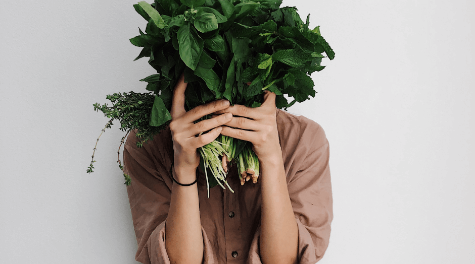 A person holding a bunch of vegetables in their hands covering their face.