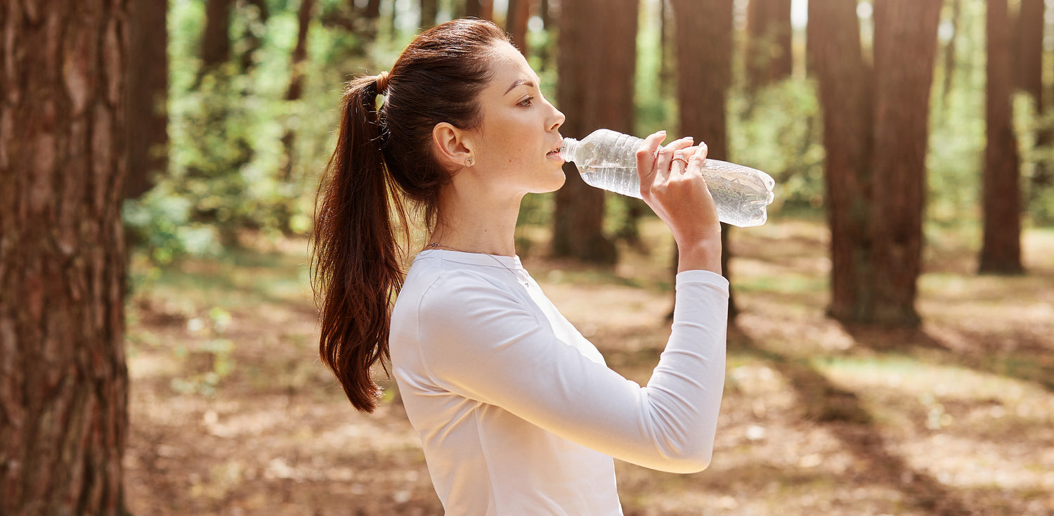 A woman drinking water from a bottle in the woods.
