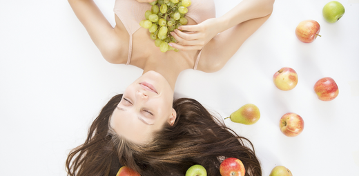 A woman laying on the ground surrounded by apples and grapes