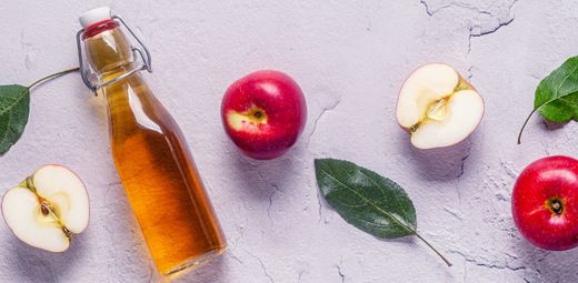 A bottle of apple cider next to apples and leaves